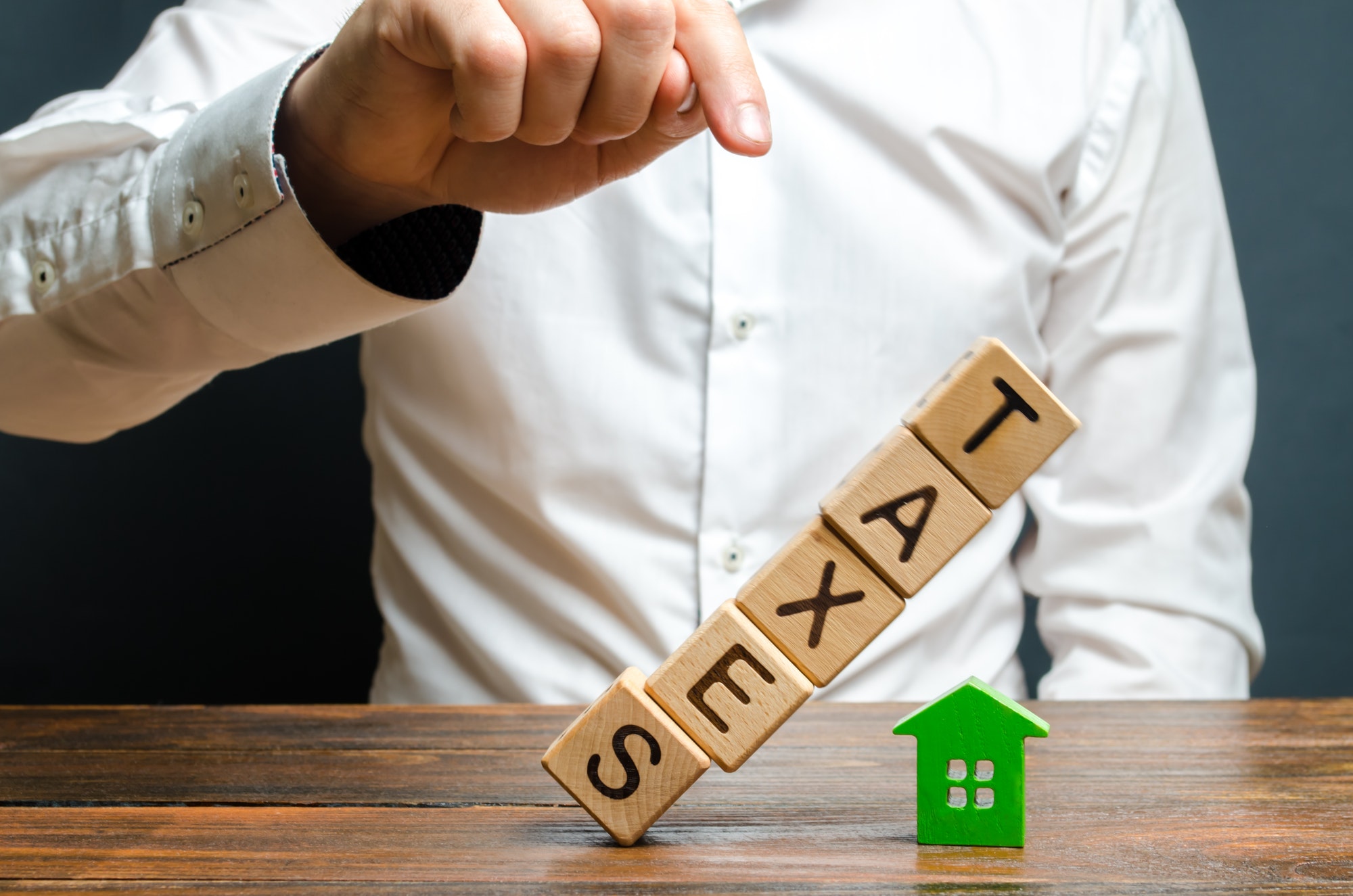 The man pushes down the tower of cubes with the word Taxes on the figure of the house